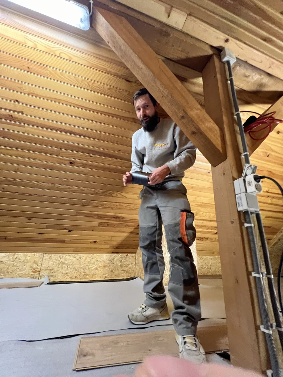 Artisan sur un chantier sous les combles, avec sous-couche et lames de parquet
